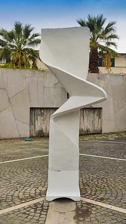 Modern geometrical sculpture located in the middle of a square. Front view. Artwork by Dado