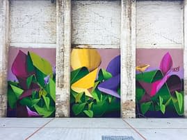 A triptych mural painting of flowers in three different colors on a white bricks wall in a wide open space, total view. Artwork by Dado