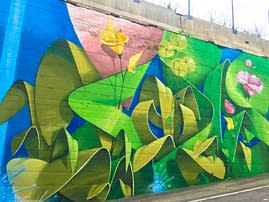 Lateral view of a Mural Painting depicting the name of the city Covignano woven with colored flowers and green leaves. Artwork by Dado