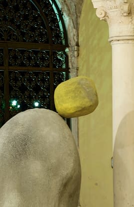 Detail of small yellow stone on top of another bigger stone, positioned in an impossible balance close to fall down the floor. Sculpture by Dado