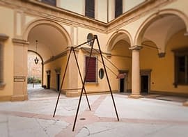 A modern sculpture consisting of an old iron swing with the seat still suspended in the air, installed in the middle of an ancient courtyard. Sculpture by Dado