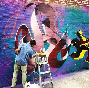 The artist Dado Ferri painting a Mural Artwork of his own tag in a spherical shape on a brick wall in New York