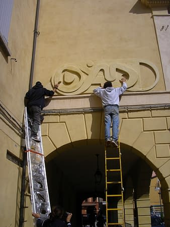 The artist Dado Ferri and his helper on a work ladder applying the bas-relief Sculpture named Lettering Medioevale on a wall for the Exhibition