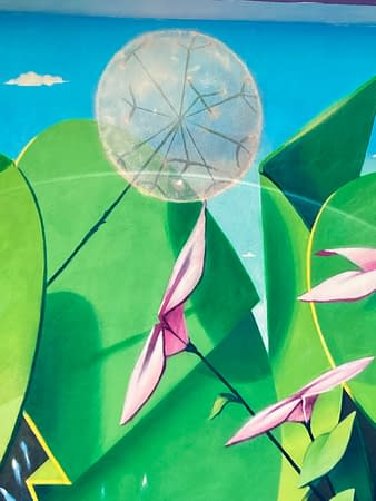 Detail of a mural painting depicting big green leaves with geometric rounded shapes, small pink flowers and a white spherical dandelion seeding head. Artwork by Dado