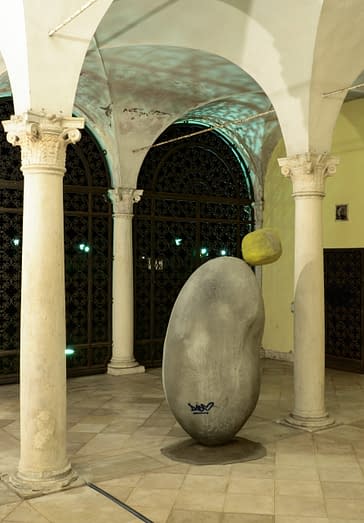 A big stone in the middle of the art gallery, with another smaller stone on top which is positioned in an impossible balance close to fall down the floor. Sculpture by Dado