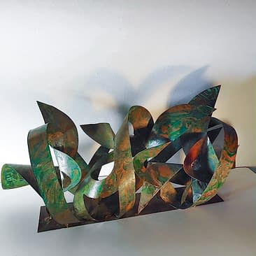 Top angle view of a sculpture made of copper ribbons sinuously coiled, forming the tag of the artist Dado. The copper colored surface is texturized with extensive green oxidation stains.