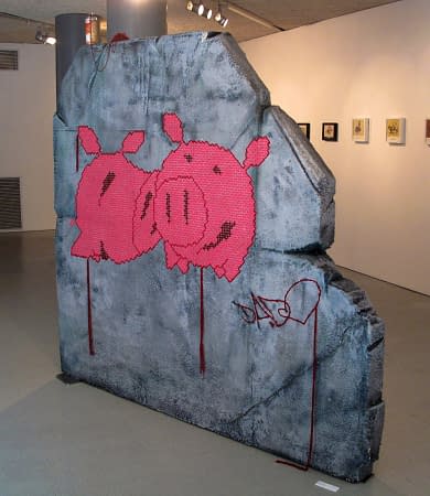 A big rock sculpture with two wool made flat pig characters stitched in the middle. Artwork by Dado