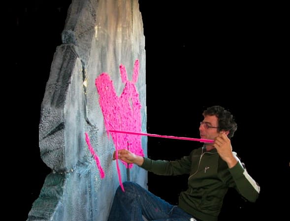 The artist Dado while stitching with a pink wool yarn a big block of something looks like a rock