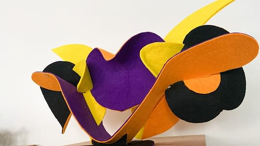 Low front view of a sculpture made of thin bent layers with a soft felt finish in a mix of high saturated yellow, orange, purple and black colors. Artwork by Dado