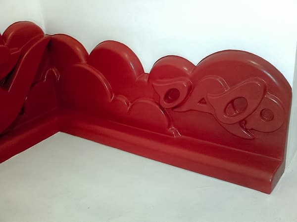 A detail of abas-relief sculpture in the form of a graffiti style baseboard all red color depicting the artist tag Dado decorated with big bubbles in the background