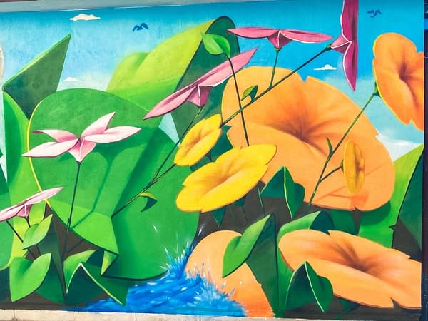Detail of a mural painting depicting big green leaves with geometric rounded shapes, big yellow-orange flowers and smaller pink and light yellow flowers floating on deep blue water. Artwork by Dado