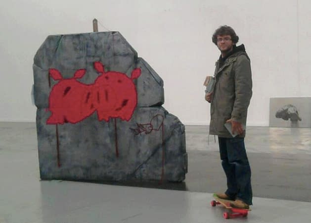 The artist Dado posing beside his own rock sculpture with two pig faced characters stitched upon.