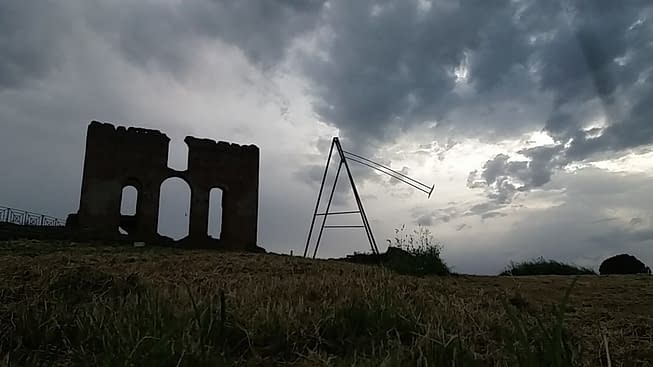 Close view of an old roman ruin beside of which is located a modern art installation consisting of an old iron swing with the seat still suspended in the air. Installation by Dado