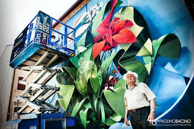 Dado painting a Graffiti-mural spherical lettering with multi colored flowers-bottom view of the entire wall and the artist on an industrial elevator