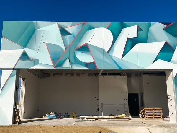 Front ground level view of a graffiti paint work on the external walls of a big building representing flat ribbons bent in geometrical shapes, light blue and white shades with thin red outlines. Artwork by Dado