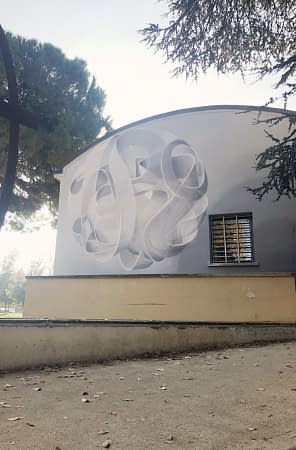 Total view of a mural painting depicting a spherical wildstyle graffiti forming the tag Dado colored in a very vanishing white and light gray tones.