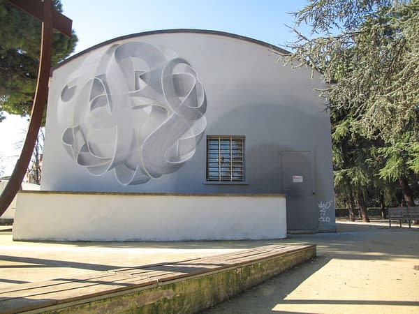 Wide view of a mural painting depicting a spherical wildstyle graffiti forming the tag Dado colored in a very vanishing white and light gray tones.