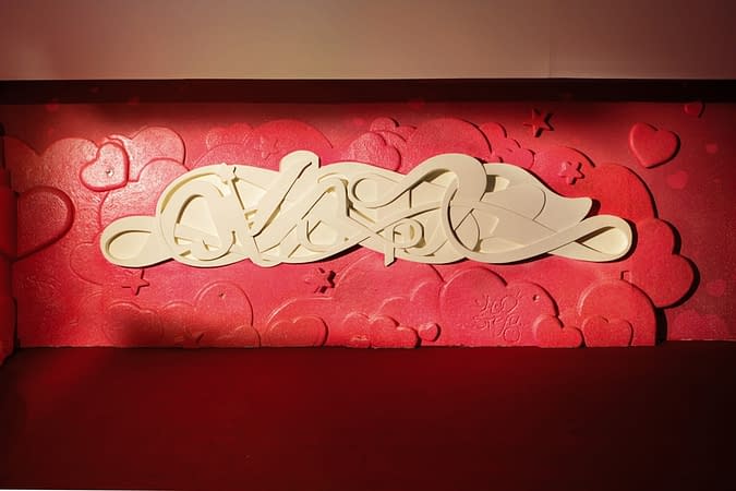 Bas-relief sculpture in a contemporary graffiti lettering plain white on pink hearted background. Front wide view Artwork by Dado