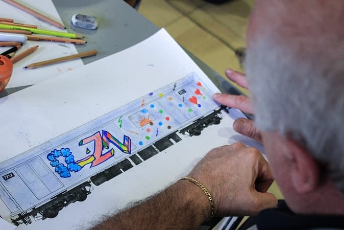 A man watching a paper sheet with a drawing depicting a train wagon with a graffiti on its side