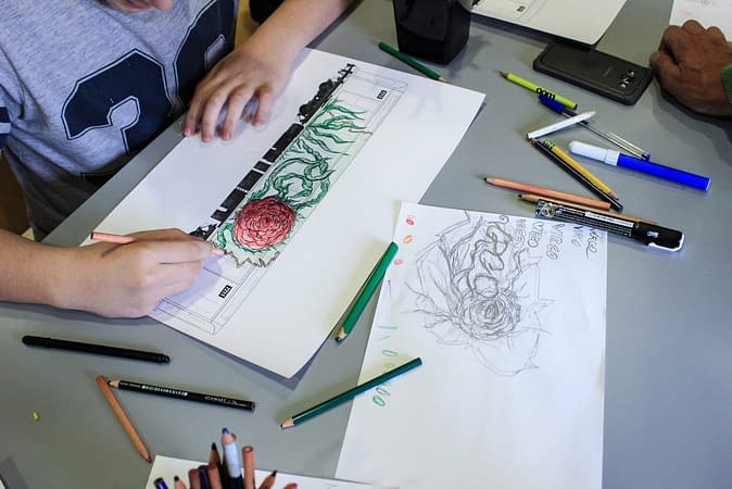 Two paper sheets on a table, upon one of them is drawing depicting a train wagon with a graffiti lettering on its side