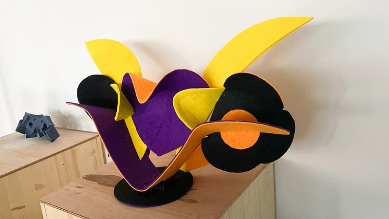 Front angle view of a sculpture made of thin bent layers with a soft felt finish in a mix of high saturated yellow, orange, purple and black colors. Artwork by Dado